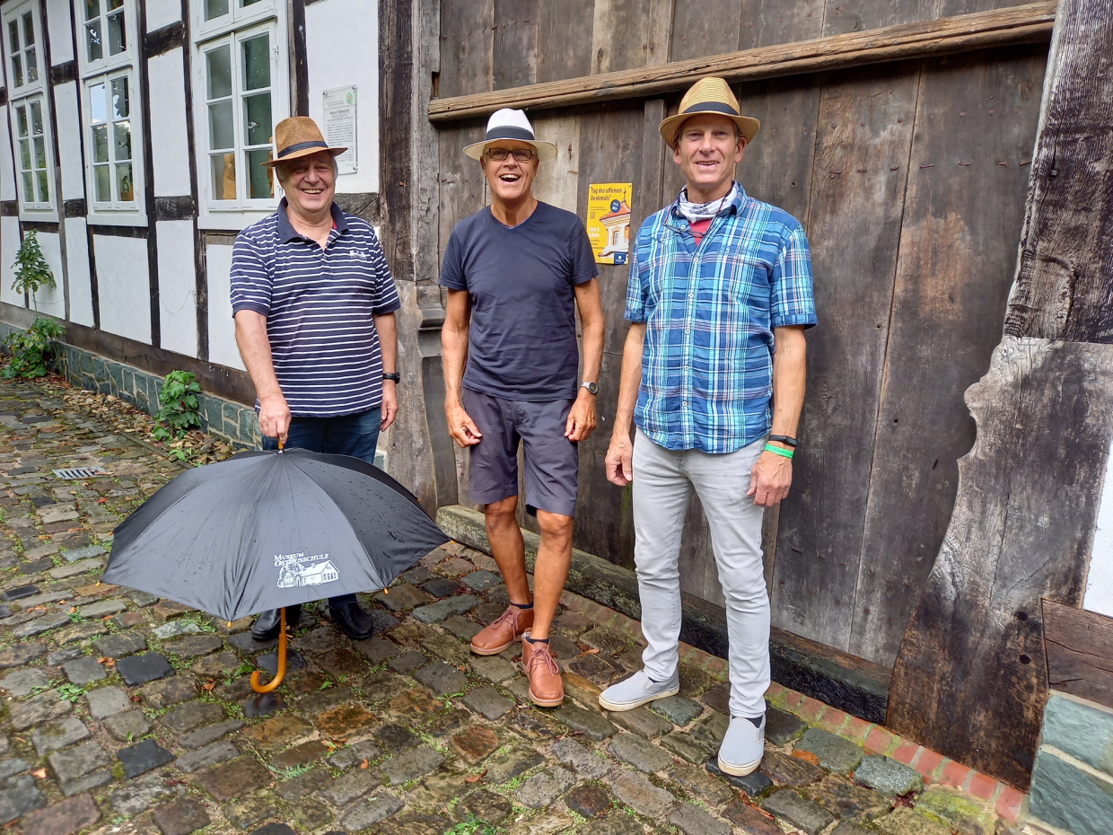 Drei Musiker mit Hut stehen vor dem Deelentor des Fachwerkhauses
