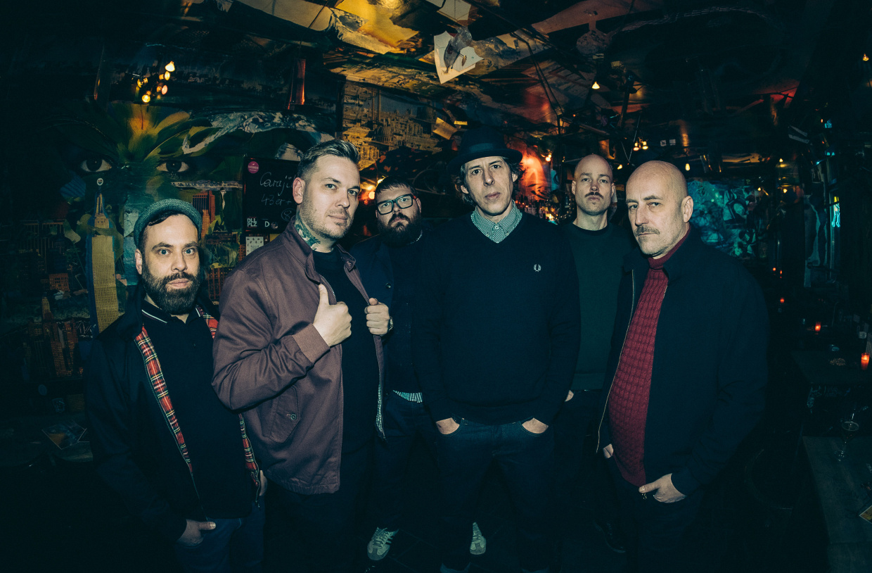 Gruppe von fünf Personen posiert zusammen in dunkler Umgebung mit warmem Licht.