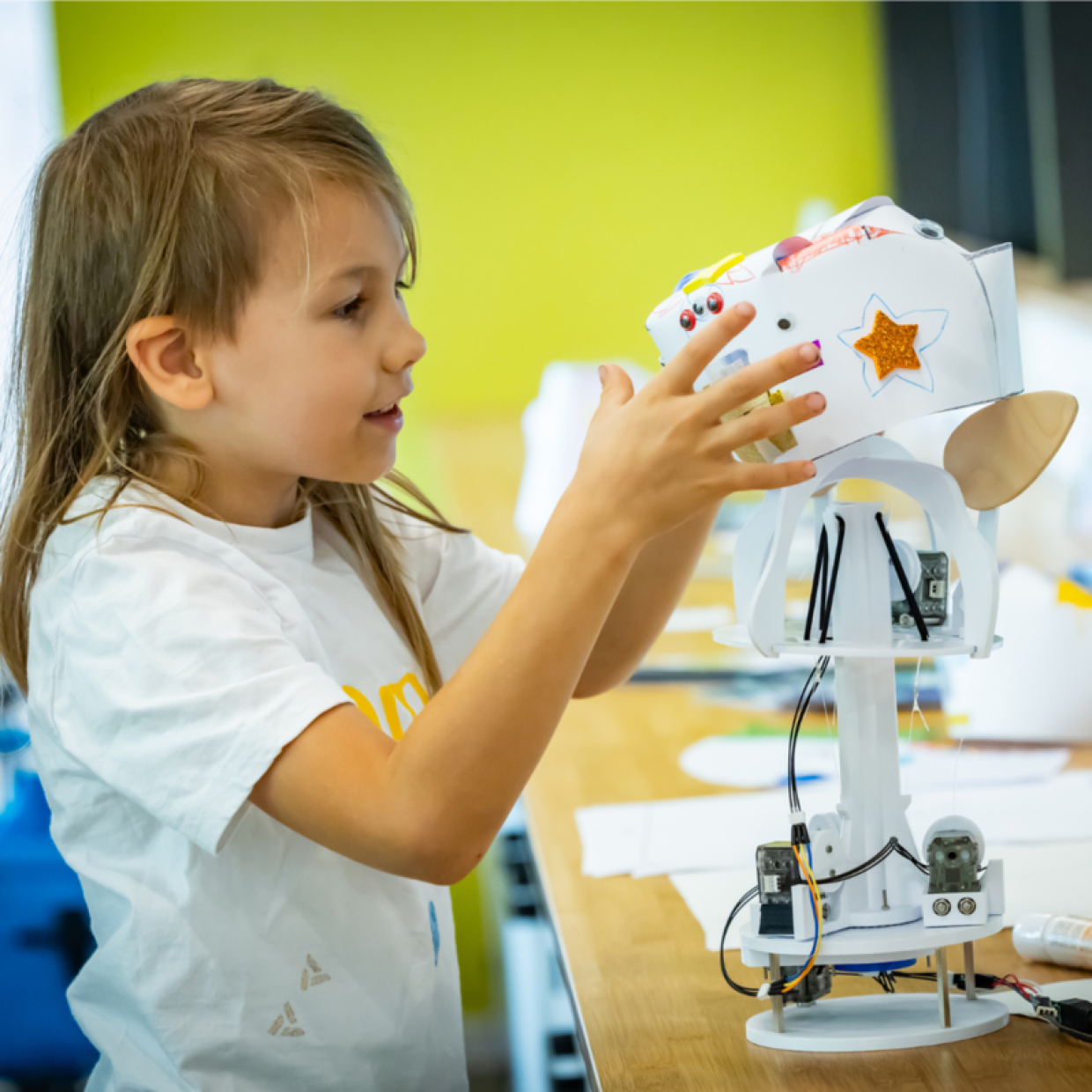 Ein Kind, dass mit seinen Händen an einen kleinen Roboter greift, der auf einen Tisch steht.
