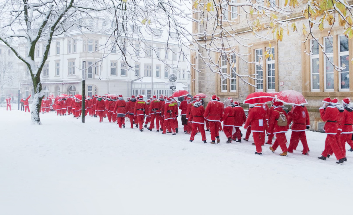 Eine große Gruppe von rot gekleideten Nikoläusen wandert durch ein winterlich verschneites Bielefeld