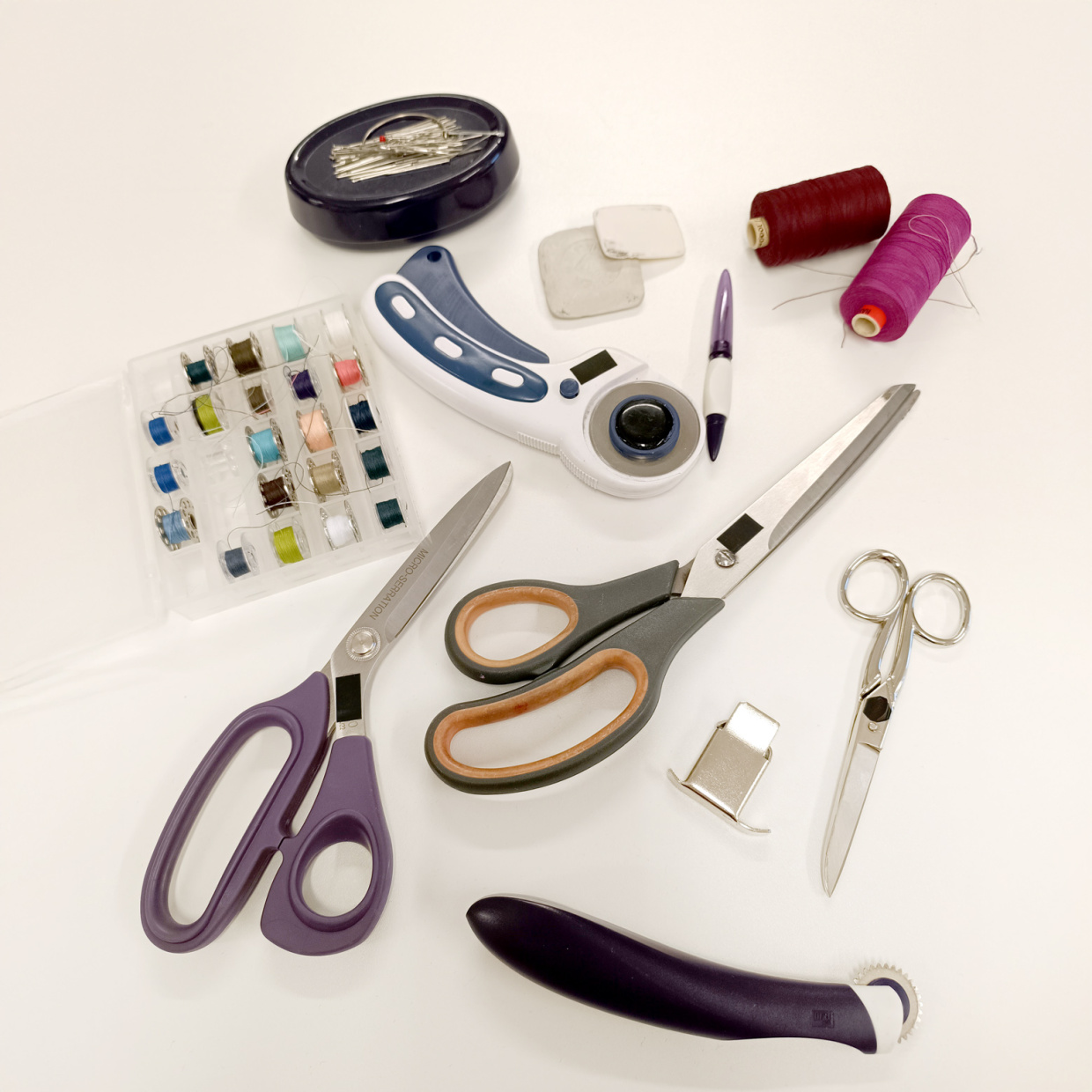 Nähmaterialien auf weißem Untergrund: Scheren, Garne, Spulen, Nadeln.