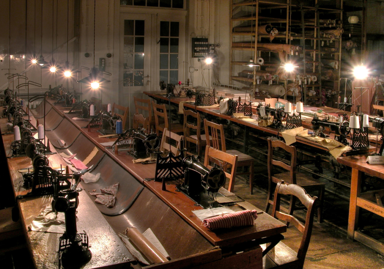 Historischer Nähsaal mit Arbeitstischen und Nähmaschinen