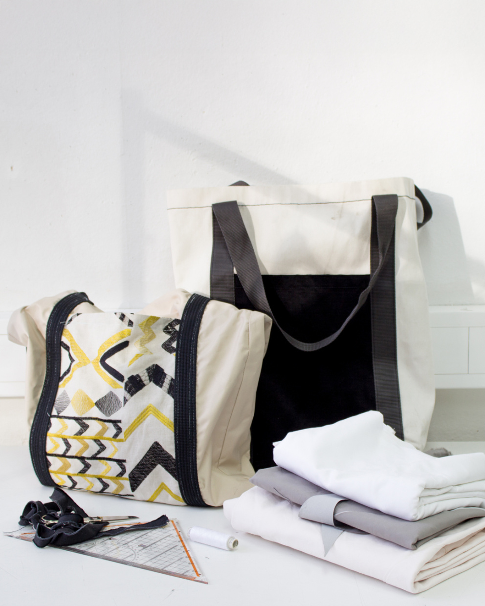 2 Shopper-Taschen vor weißem Hintergrund. Davor liegen Stoffe und Nähutensilien.