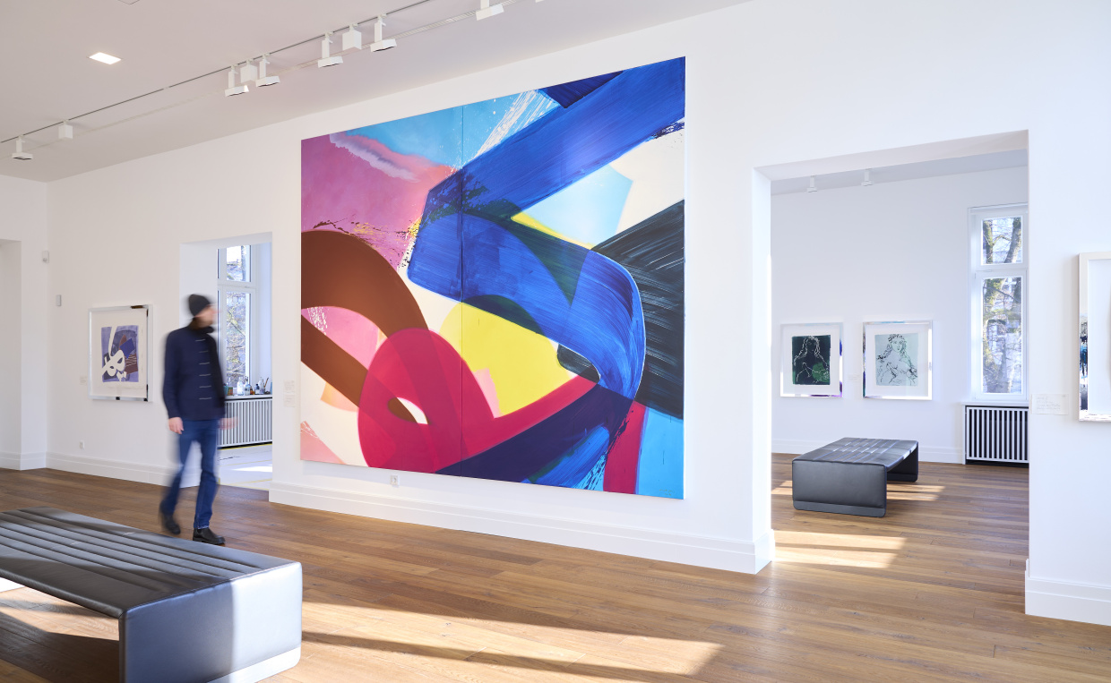 Eine farbenfrohe, große Malerei im Museum, an der ein Mensch vorbeigeht.