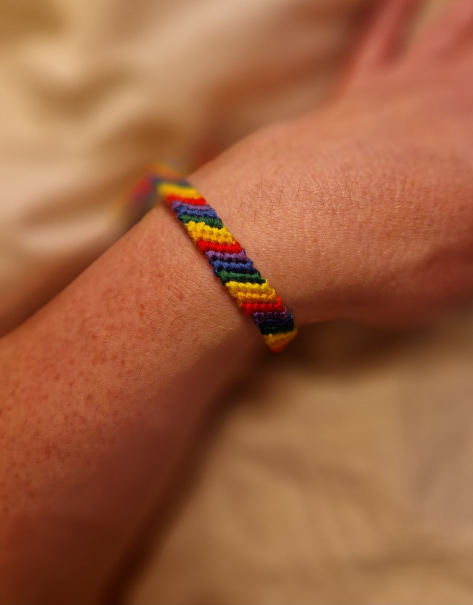 Das Bild zeigt ein geknüpftes Armband in Regenbogenfarben an einem Handgelenk.