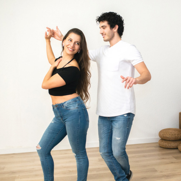 Frau und Mann tanzen gemeinsam in hellem Raum, beide tragen Jeans und T-Shirts.