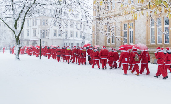 Eine große Gruppe von rot gekleideten Nikoläusen wandert durch ein winterlich verschneites Bielefeld