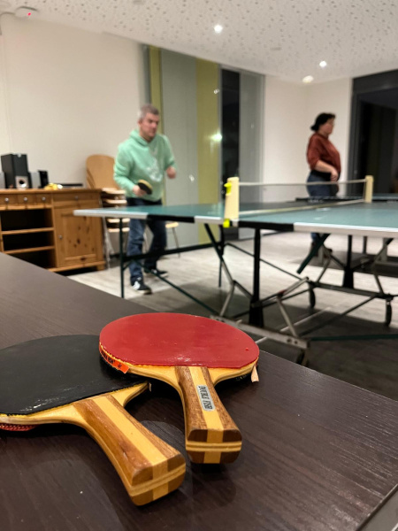 zwei Tischtennisschläger auf einem Tisch liegend und im Hintergrund spielen Personen Tischtennis