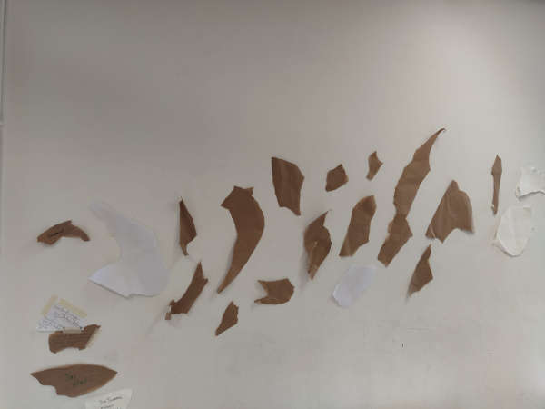 weiße und braune Schnipsel aus Papier an einer langen weißen Wand befestigt