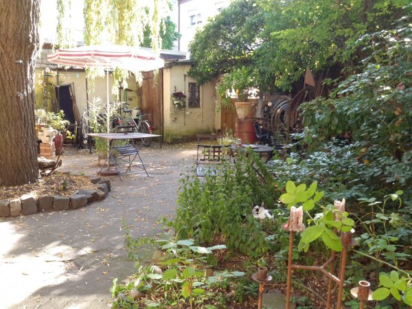 Ein Blick in den Innenhof der akw: Gegenüber ist der Eingang, links steht ein Baum, Weg in der Mitte