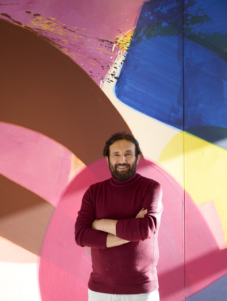 Der Künstler Aatifi steht vor einer großen, farbenfrohen Malerei