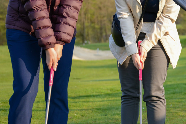 Zwei Personen stehen auf einem Golfplatz und halten jeweils einen Golfschläger. 