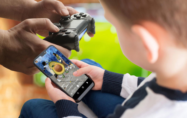 Ein Kind spielt auf einem Smartphone, Hände mit Controller einer Spielekonsole