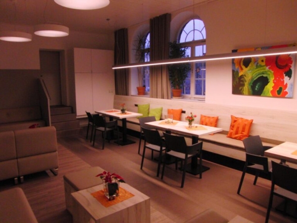 Gemütlicher Raum mit einem langen Sofa voller Kissen, Tischen und Stühlen zum Verweilen