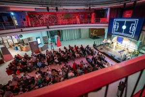 Im Oval der Wissenswerkstadt ist eine Bühne aufgebaut und die zahlreichen Sitzreihen sind voll besetzt.