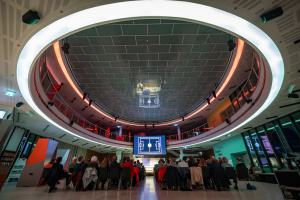 Veranstaltung in der Wissenswerkstadt Bielefeld: Zuschauer blicken in einem modernen, oval beleuchteten Raum auf eine Bühne mit einer Leinwand, auf der ein Spielfeld abgebildet ist.