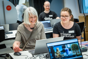 3. Eine Teilnehmerin und eine betreuende Person arbeiten gut gelaunt an einem Laptop in der Wissenswerkstadt.