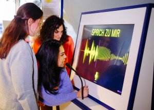 Drei Besucherinnen testen eine Mitmachstation, an der Sprache über ein Mikrofon sichtbar gemacht wird.