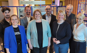 Gruppe steht zusammen in der Ausstellung und lächelt in die Kamera.