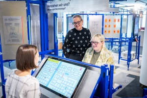 Drei Frauen an einem Ausstellungsmodul mit einem großen Bildschirm